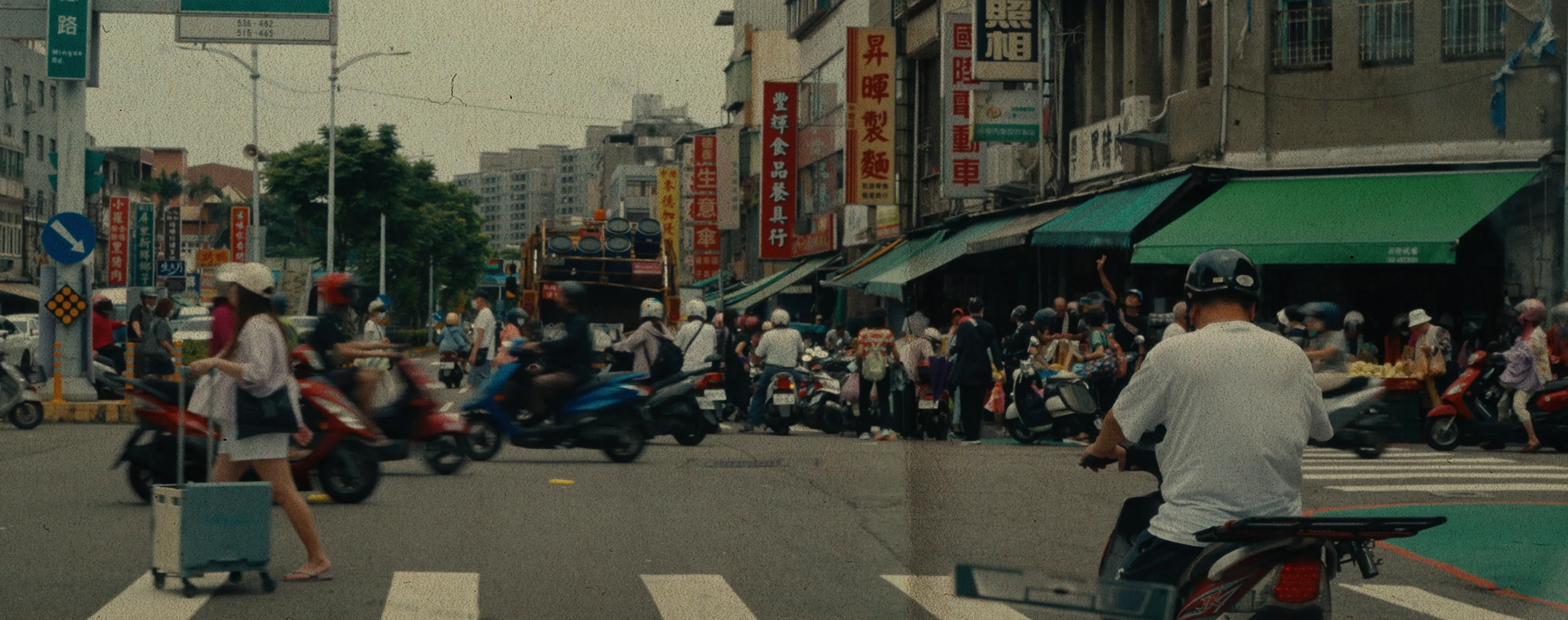 菜市場的十字路口,往來的摩托車與行人穿越馬路的景象。