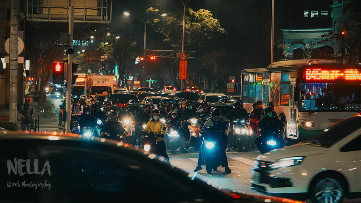 夜間街道擠滿等待通行的機車騎士,紅綠燈與店家招牌照亮路口