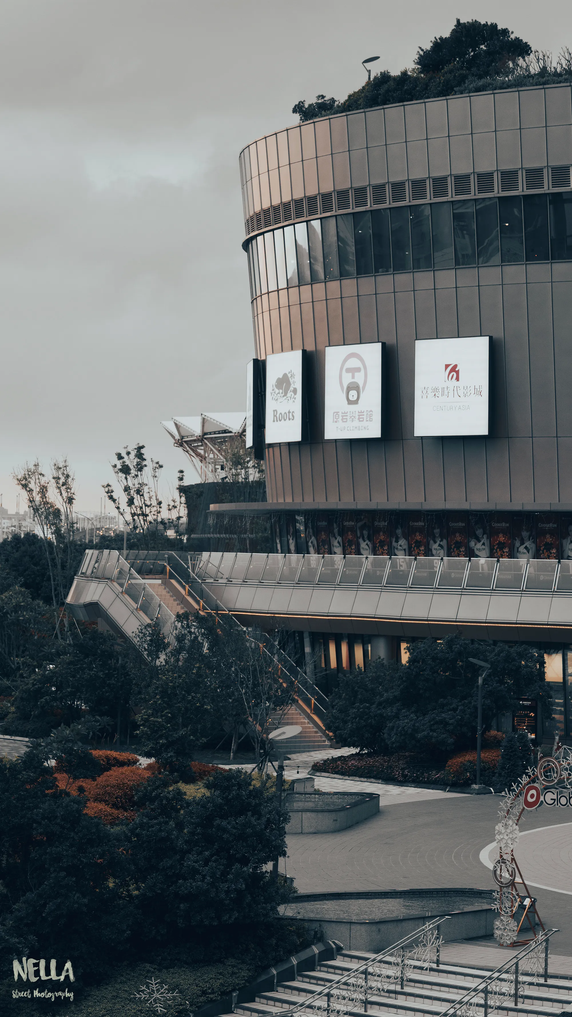 灰色天空下的圓形建築立面,前方排列數面方形招牌與光禿樹枝