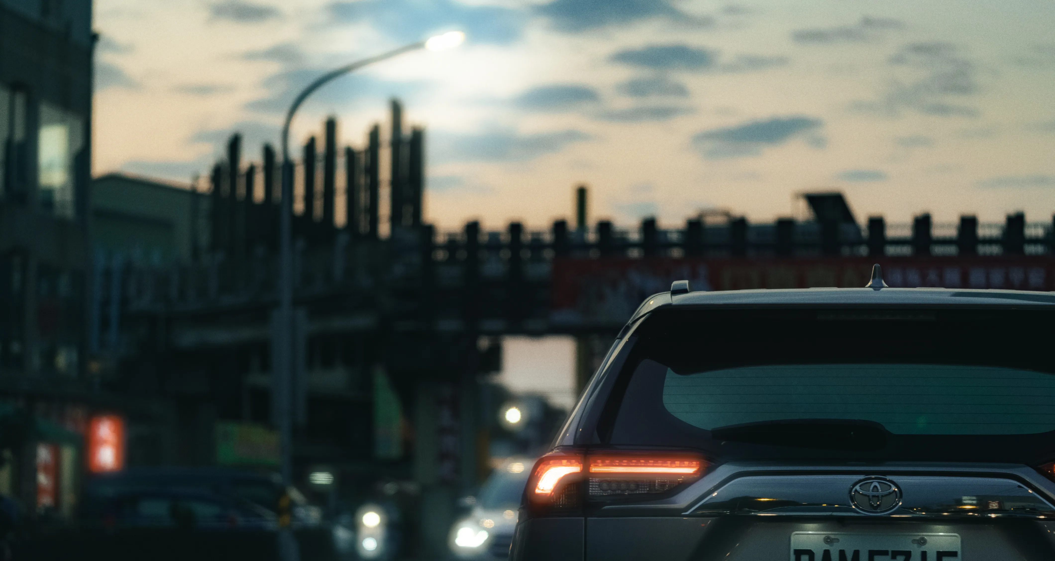 黃昏道路上的汽車車流近景,遠處建築與欄杆在雲層下形成剪影