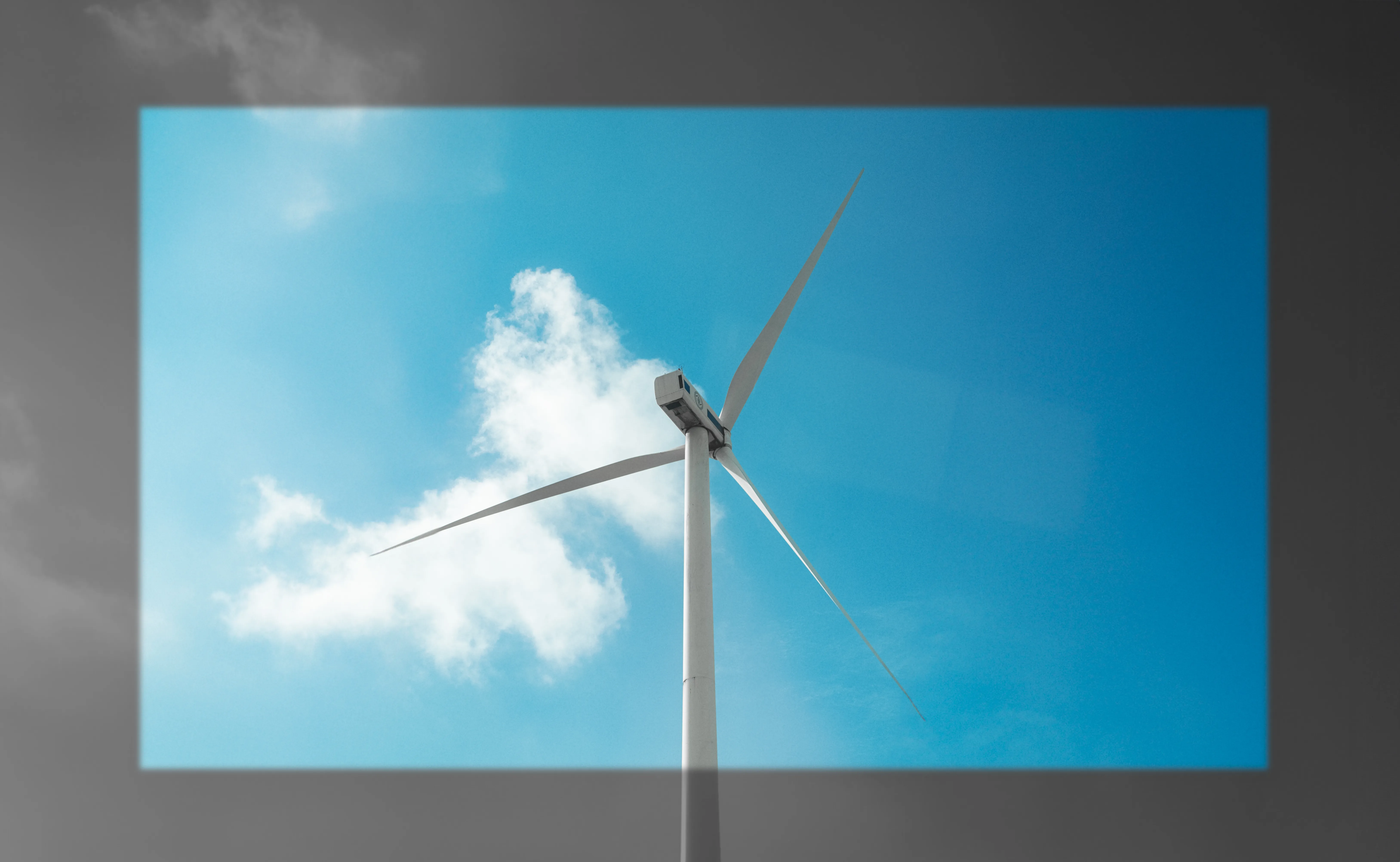 白色風力發電機立在藍天與白雲前,畫面四周帶有深灰色邊框